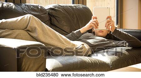 Girl laying on sofa reading digital tablet View Large Photo Image Stock Image - Girl laying on sofa reading digital tablet. Fotosearch