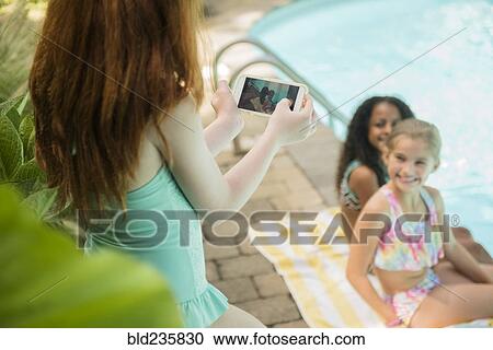 Girl photographing friends with cell phone at swimming pool View Large Photo Image Stock Image - Girl photographing friends with cell phone at swimming pool. Fotosearch