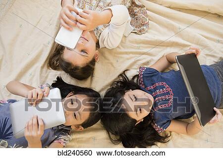 Girls laying on blanket using cell phone and digital tablets View Large Photo Image Stock Image - Girls laying on blanket using cell phone and digital tablets. Fotosearch