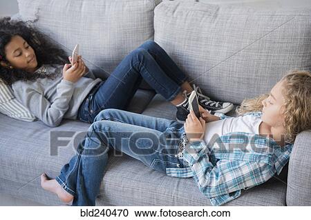 Girls laying on sofa texting on cell phones View Large Photo Image Stock Image - Girls laying on sofa texting on cell phones. Fotosearch