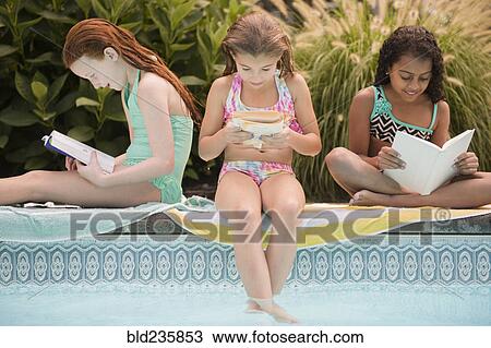 Stock Image - Girls reading books at the edge of swimming pool. Fotosearch