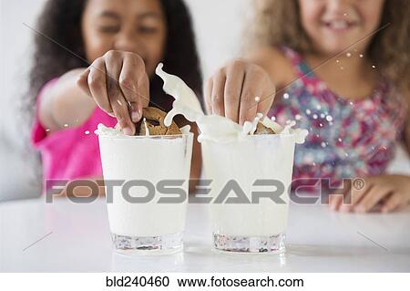 Girls splashing cookies in glasses of milk View Large Photo Image Stock Image - Girls splashing cookies in glasses of milk. Fotosearch