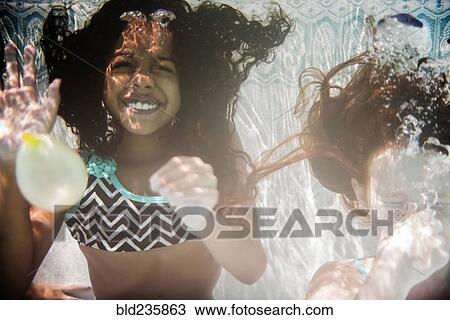 Stock Image - Girls swimming and waving underwater. Fotosearch