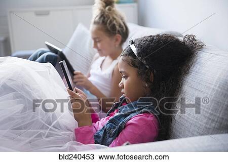 Girls using digital tablets on sofa View Large Photo Image Stock Image - Girls using digital tablets on sofa. Fotosearch