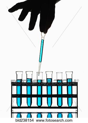 Picture - Hand holding pipette dripping blue liquid into test tubes. Fotosearch