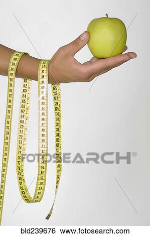 Hand of Caucasian woman holding green apple and measuring tape View Large Photo Image Stock Photograph - Hand of Caucasian woman holding green apple and measuring tape. Fotosearch