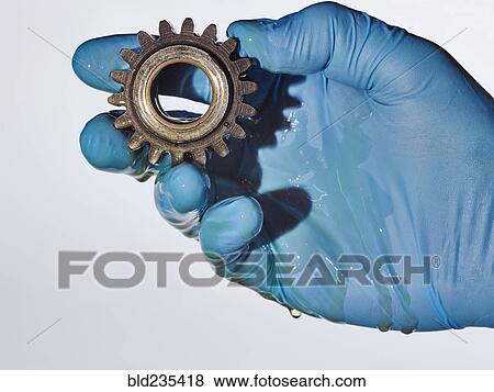 Stock Photo - Hand wearing rubber-glove holding gear dripping with oil. Fotosearch