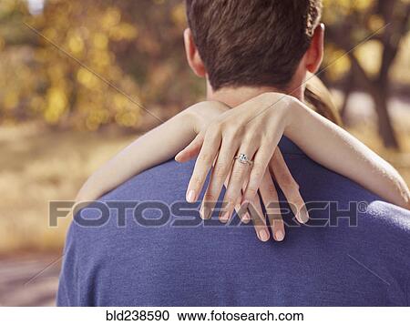 Stock Image - Hands of woman wearing engagement ring hugging man. Fotosearch