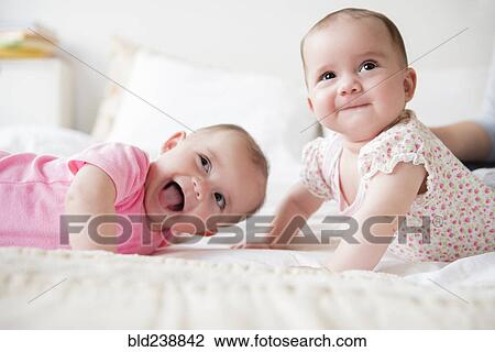 Stock Image - Happy Caucasian twin baby girls on bed. Fotosearch
