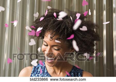 Stock Photograph - Heart-shape confetti falling on smiling Black woman . Fotosearch