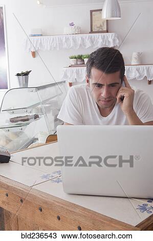 Stock Image - Hispanic baker using laptop and cell phone. Fotosearch