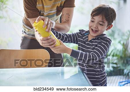Stock Photo - Hispanic boy helping father spray cleaner on table. Fotosearch