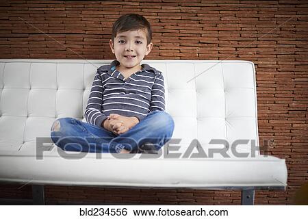 Stock Photograph - Hispanic boy sitting cross-legged on sofa. Fotosearch