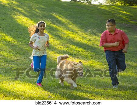 Picture - Hispanic brother and sister running with dog on hill. Fotosearch