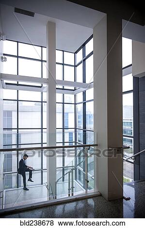Hispanic businessman sitting on staircase railing near window View Large Photo Image Stock Photo - Hispanic businessman sitting on staircase railing near window. Fotosearch