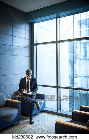 Stock Image - Hispanic businessman writing on notepad in office lounge. Fotosearch