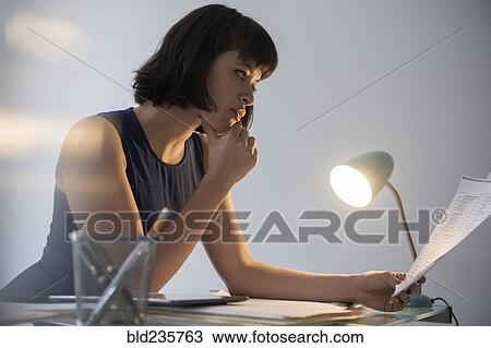 Stock Image - Hispanic businesswoman working late reading paperwork. Fotosearch