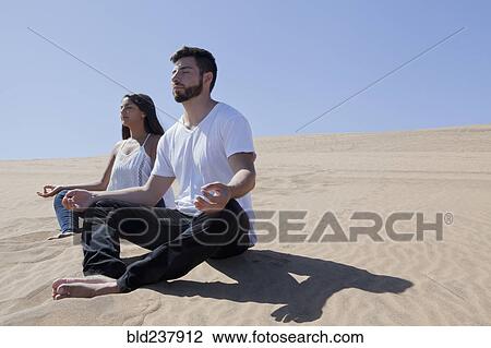 Stock Image - Hispanic couple meditating at beach. Fotosearch