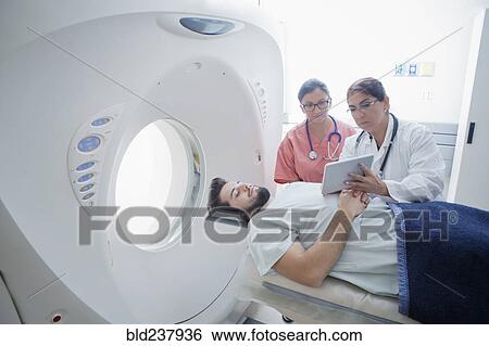 Stock Photograph - Hispanic doctor and nurse showing digital tablet to patient at scanner. Fotosearch