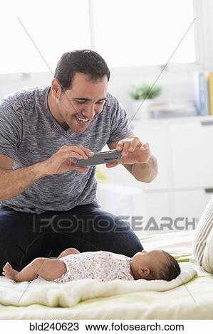 Hispanic father on bed photographing baby daughter with cell phone View Large Photo Image Stock Image - Hispanic father on bed photographing baby daughter with cell phone. Fotosearch