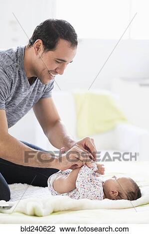 Stock Image - Hispanic father on bed playing with baby daughter. Fotosearch