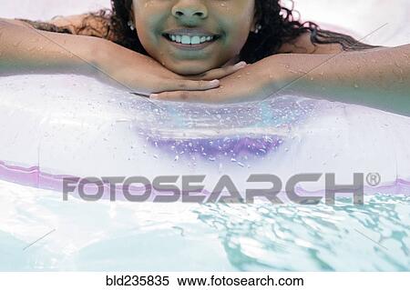 Stock Photography - Hispanic girl floating on inflatable ring in swimming pool. Fotosearch