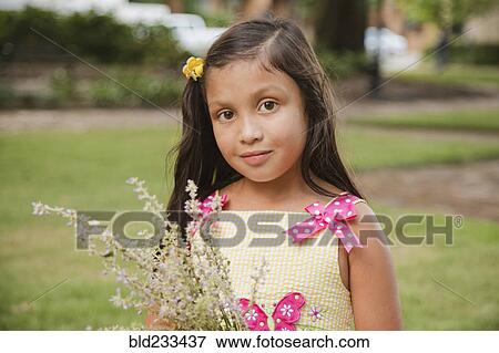 Stock Photo - Hispanic girl holding flowers in park. Fotosearch