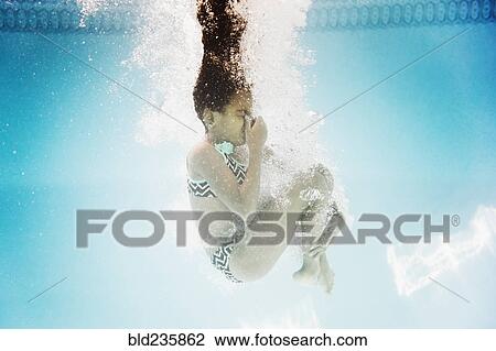 Stock Image - Hispanic girl swimming underwater holding nose. Fotosearch