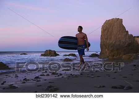 Hispanic man carrying surfboard on beach at sunset View Large Photo Image Stock Image - Hispanic man carrying surfboard on beach at sunset. Fotosearch