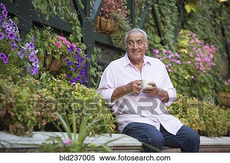 Stock Photography - Hispanic man drinking coffee in flower garden. Fotosearch
