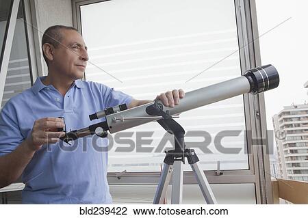 Stock Image - Hispanic man holding telescope near window. Fotosearch