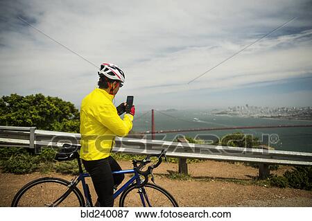 Hispanic man on bicycle photographing waterfront with cell phone View Large Photo Image Stock Photo - Hispanic man on bicycle photographing waterfront with cell phone. Fotosearch