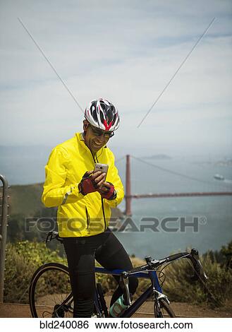Hispanic man on bicycle texting on cell phone at waterfront View Large Photo Image Stock Photograph - Hispanic man on bicycle texting on cell phone at waterfront. Fotosearch
