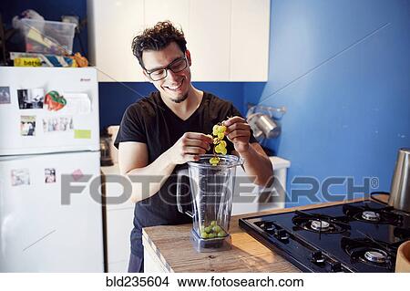Picture - Hispanic man putting grapes in blender. Fotosearch