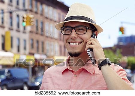 Stock Image - Hispanic man talking on cell phone in city. Fotosearch