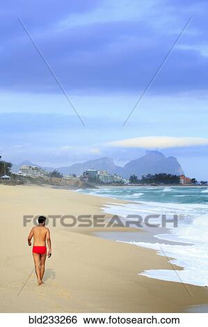 Stock Photograph - Hispanic man walking on beach near waves. Fotosearch
