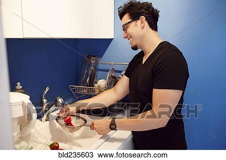 Stock Image - Hispanic man washing strawberries in sink. Fotosearch