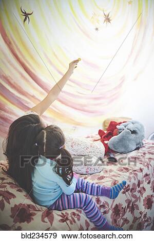 Stock Photo - Hispanic mother and daughter on bed looking at mural on wall. Fotosearch
