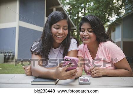 Stock Photo - Hispanic mother and daughter texting on cell phone near apartments. Fotosearch