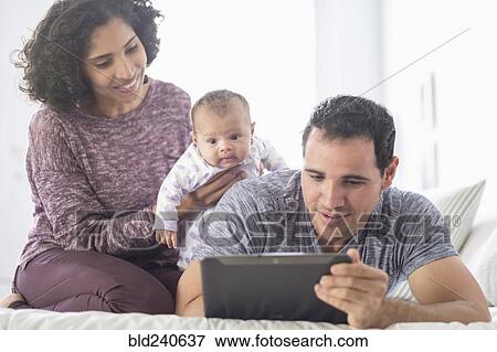 Stock Photo - Hispanic mother and father with baby daughter watching digital tablet. Fotosearch