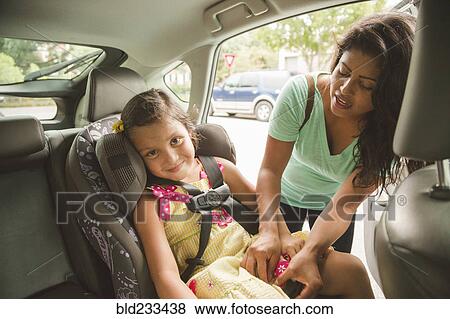 Stock Photo - Hispanic mother buckling daughter in car seat. Fotosearch