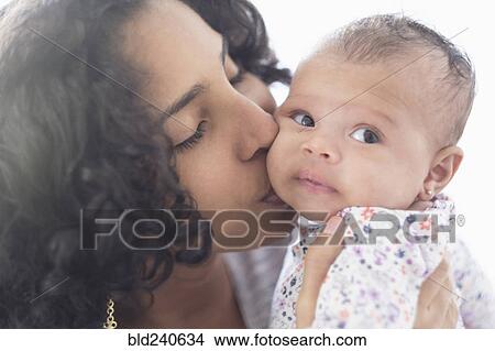 Picture - Hispanic mother kissing baby daughter on cheek. Fotosearch