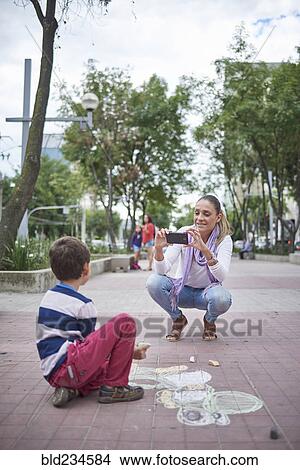 Hispanic mother photographing son on sidewalk View Large Photo Image Picture - Hispanic mother photographing son on sidewalk. Fotosearch