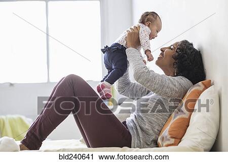 Stock Image - Hispanic mother playing with baby daughter on bed. Fotosearch