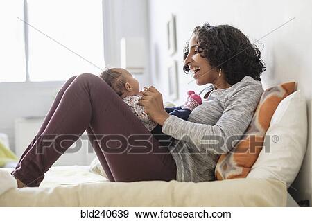 Stock Photo - Hispanic mother playing with baby daughter on bed. Fotosearch
