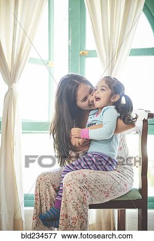 Stock Photo - Hispanic mother sitting in chair holding laughing daughter. Fotosearch