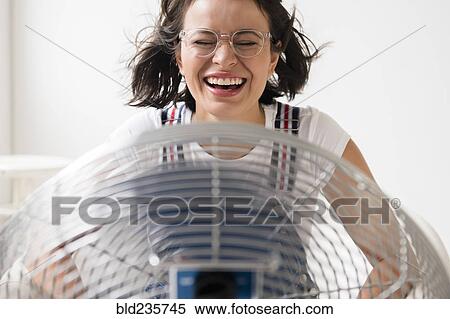 Stock Photography - Hispanic woman cooling off using fan. Fotosearch