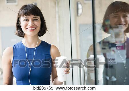 Stock Photography - Hispanic woman drinking coffee and listening to earbuds. Fotosearch