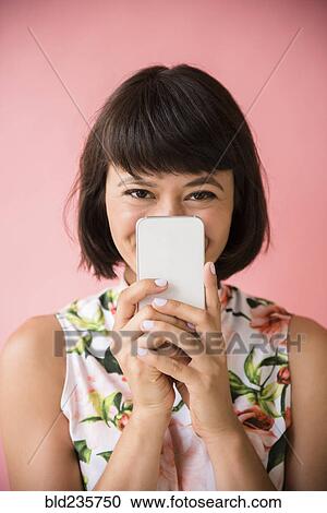 Stock Image - Hispanic woman hiding face behind cell phone. Fotosearch