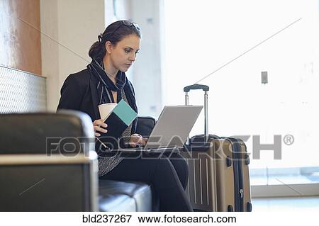 Stock Photo - Hispanic woman holding passport using laptop in airport. Fotosearch